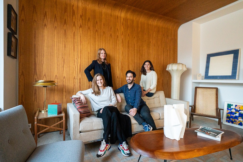 Photo d'équipe avec 4 personnes posant dans un bureau au mur et plafond en bois et oeuvres d'art