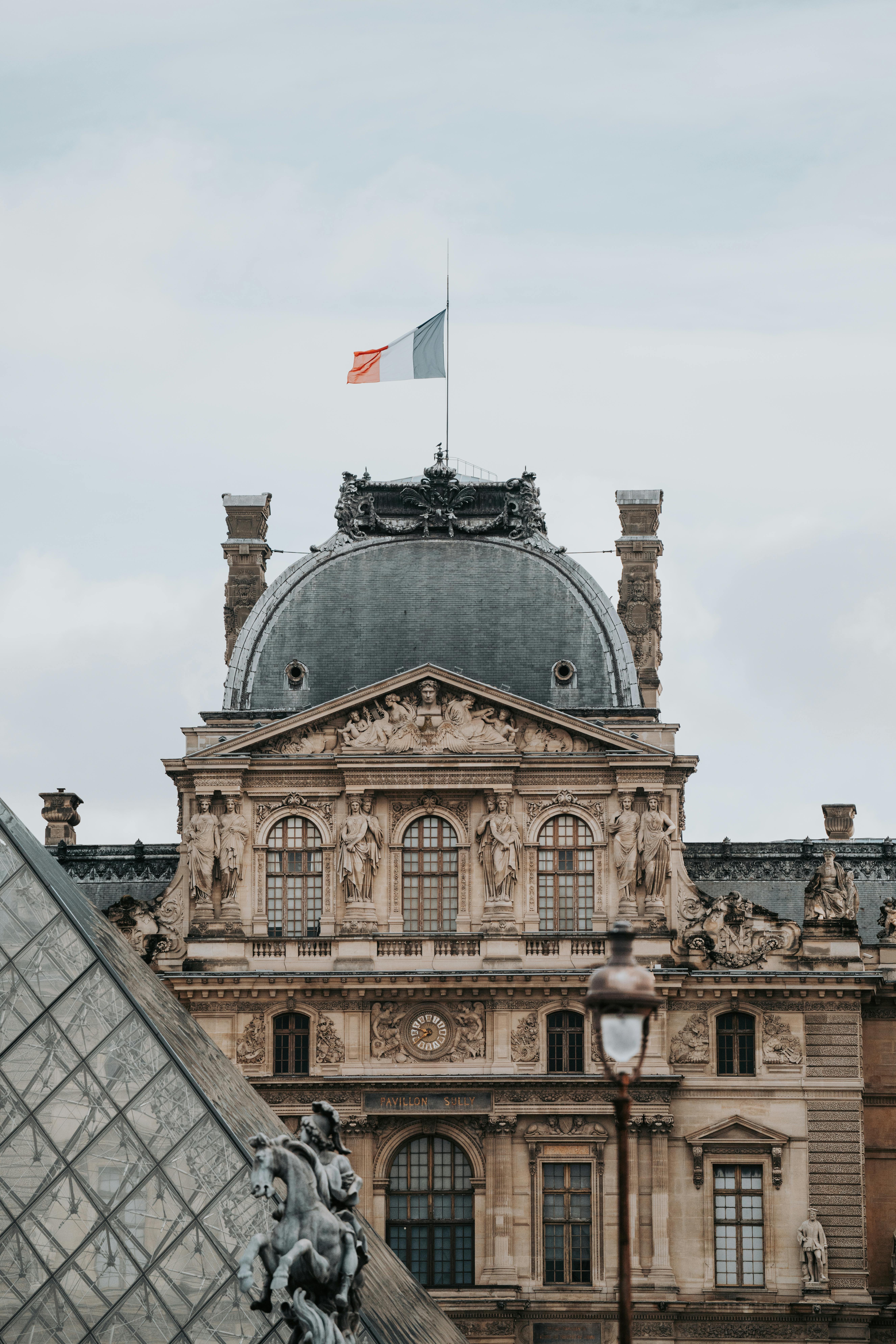 Détails architecturaux de la façade du Louvre à Paris avec le drapeau français sur le toit et au premier plan un bout de la pyramide de verre