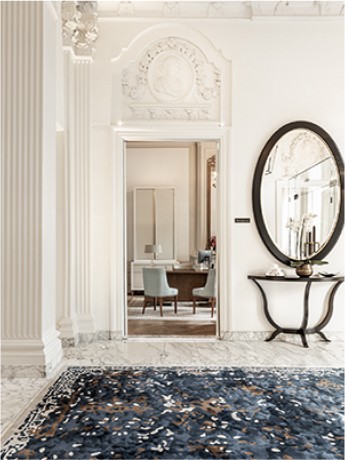 Enfilade de salon avec une très grande hauteur sous plafond, des moulures haussmanniennes et un sol en marbre orné d'un grand tapis indigo. La pièce comprend également une sellette art déco et un grand miroir ovale.